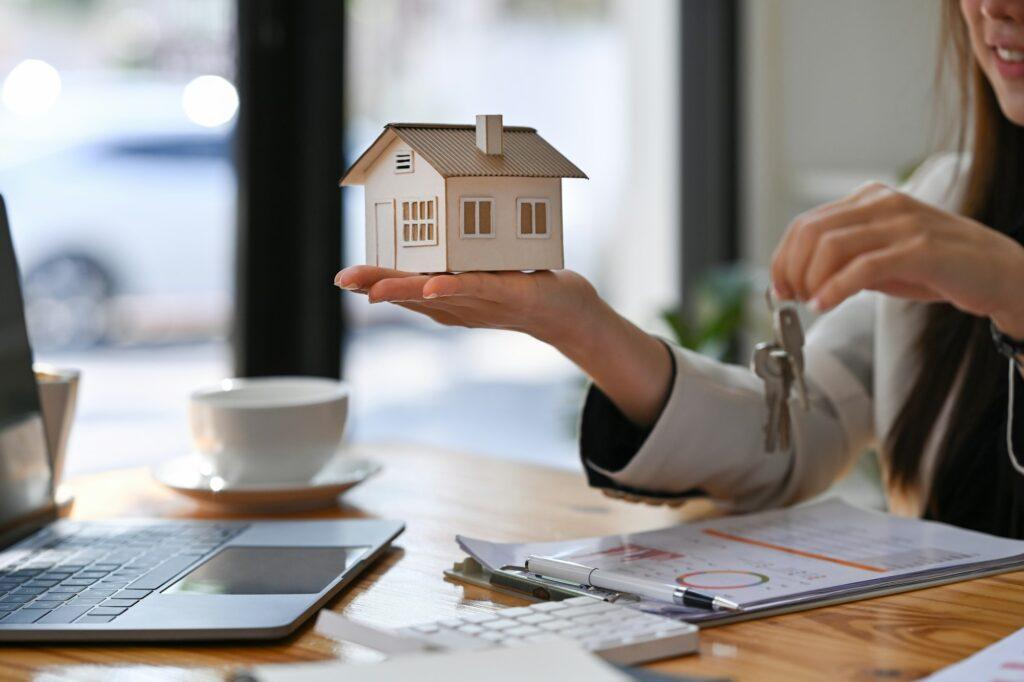 Estate agent holding house model and house key in hand.